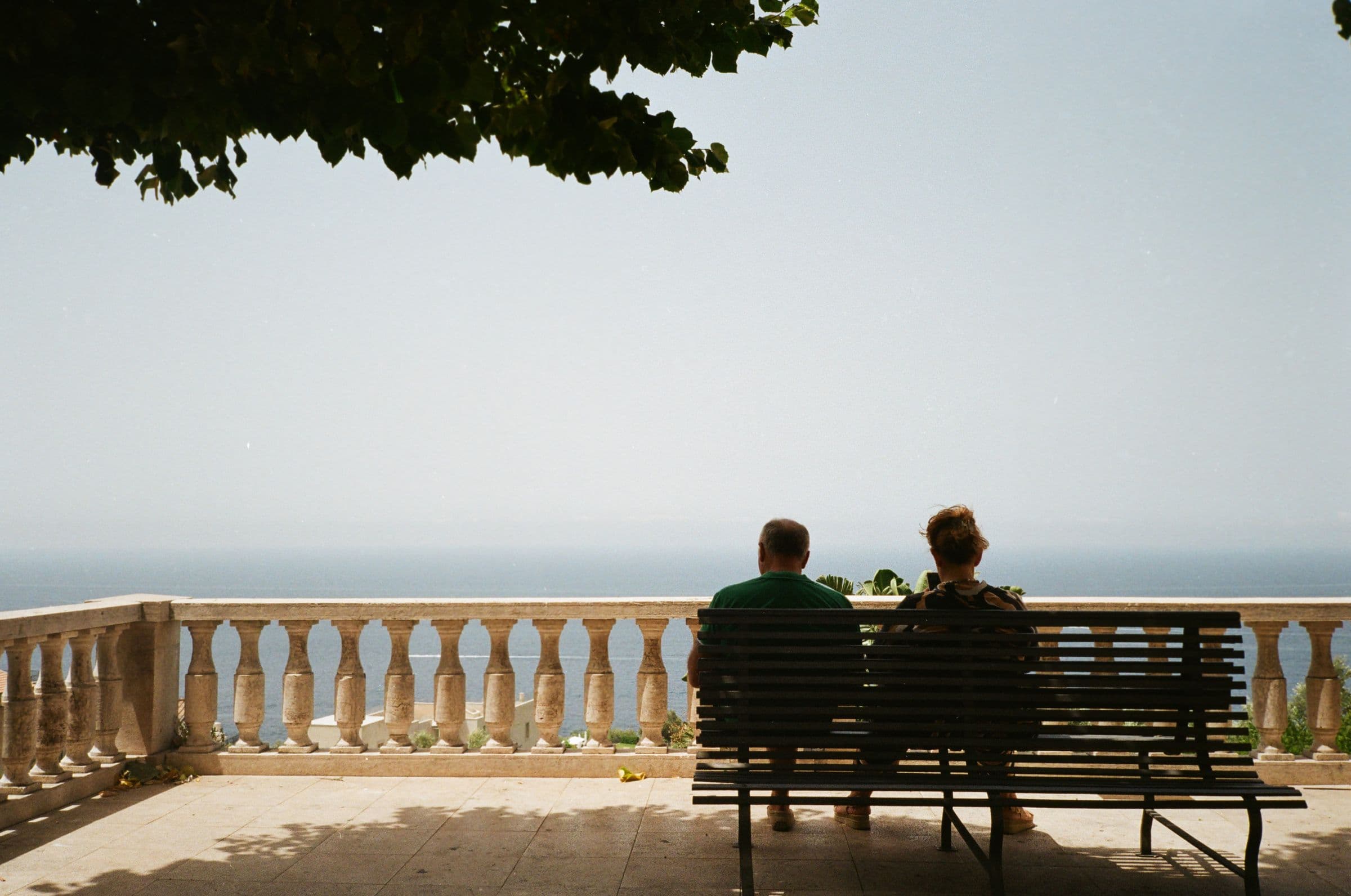 Two people on a bench on a terrace, looking out at the sea
