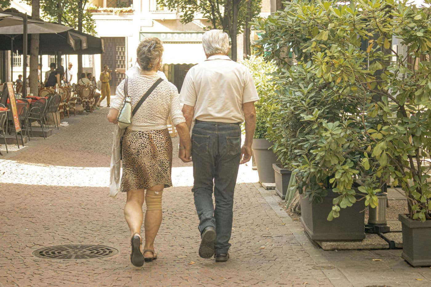 An older couple walking hand in hand down a street in Italy